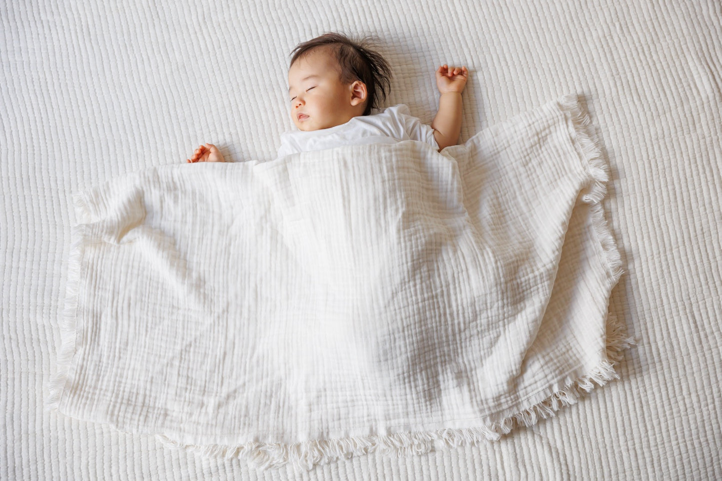 A 100% cotton crinkle blanket gently wraps around a sleeping baby.