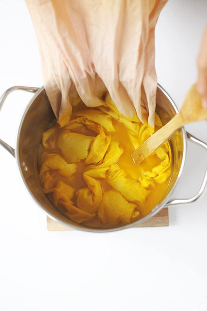 Cotton fabric dyeing in a bright yellow natural dye bath (weld / Reseda luteola) in a stainless steel pot.