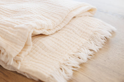 Close-up of undyed 4-layer crinkled cotton muslin fabric showing textured weave and fringed edge, dye-ready for natural dyeing